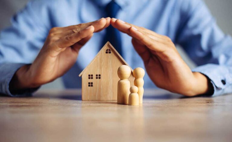 A homeowner reviews insurance documents and a credit report at a kitchen table with a laptop and calculator.